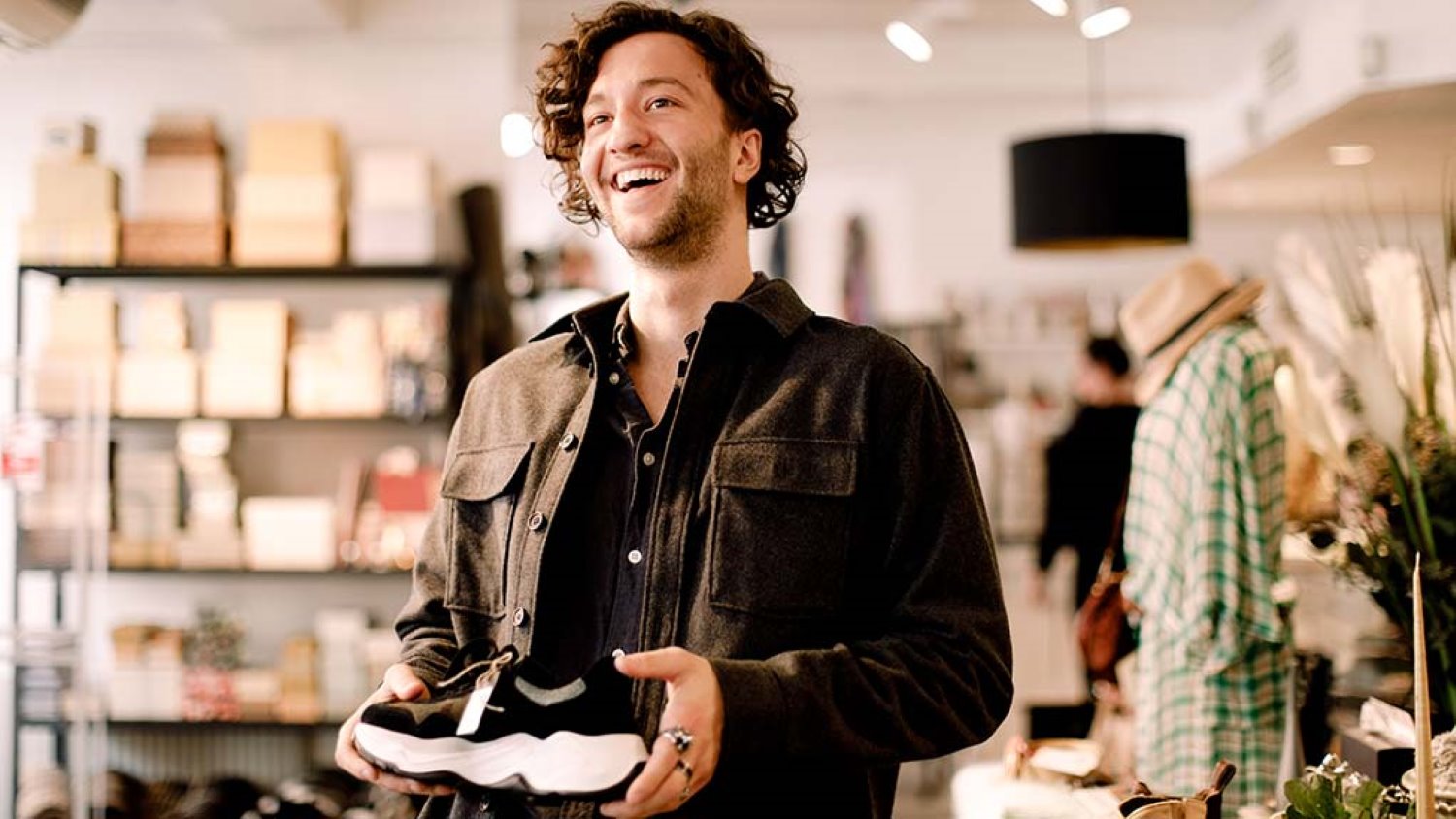 Kiharatukkainen mies hymyilee ostamassa kenkiä