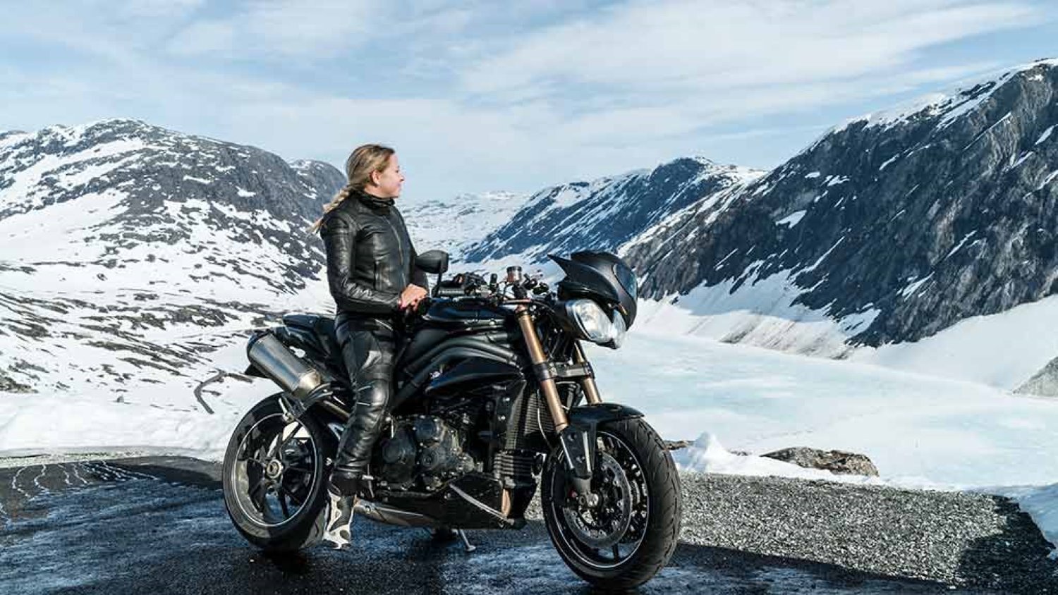 Nainen istuu moottoripyörän päällä ja ihailee Norjan vuoristoa