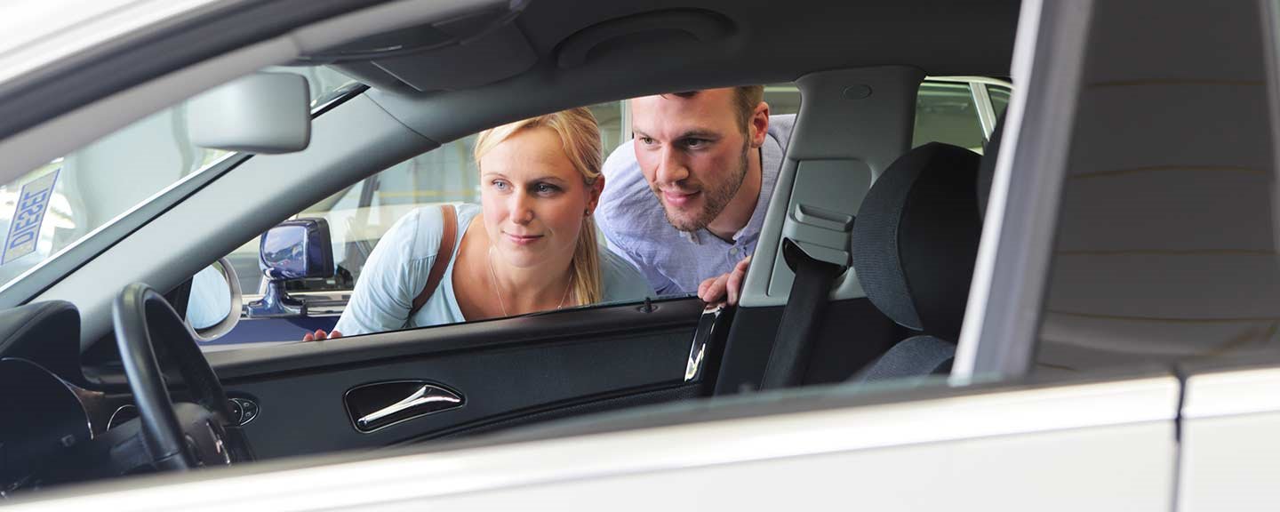 Pariskunta katselee uutta valkoista autoa autoliikkeessä