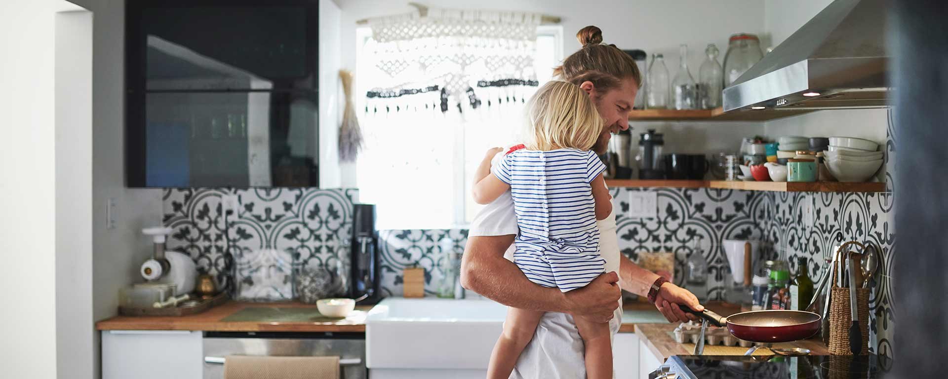 Mies kokkaa lapsi sylissä keittiössä