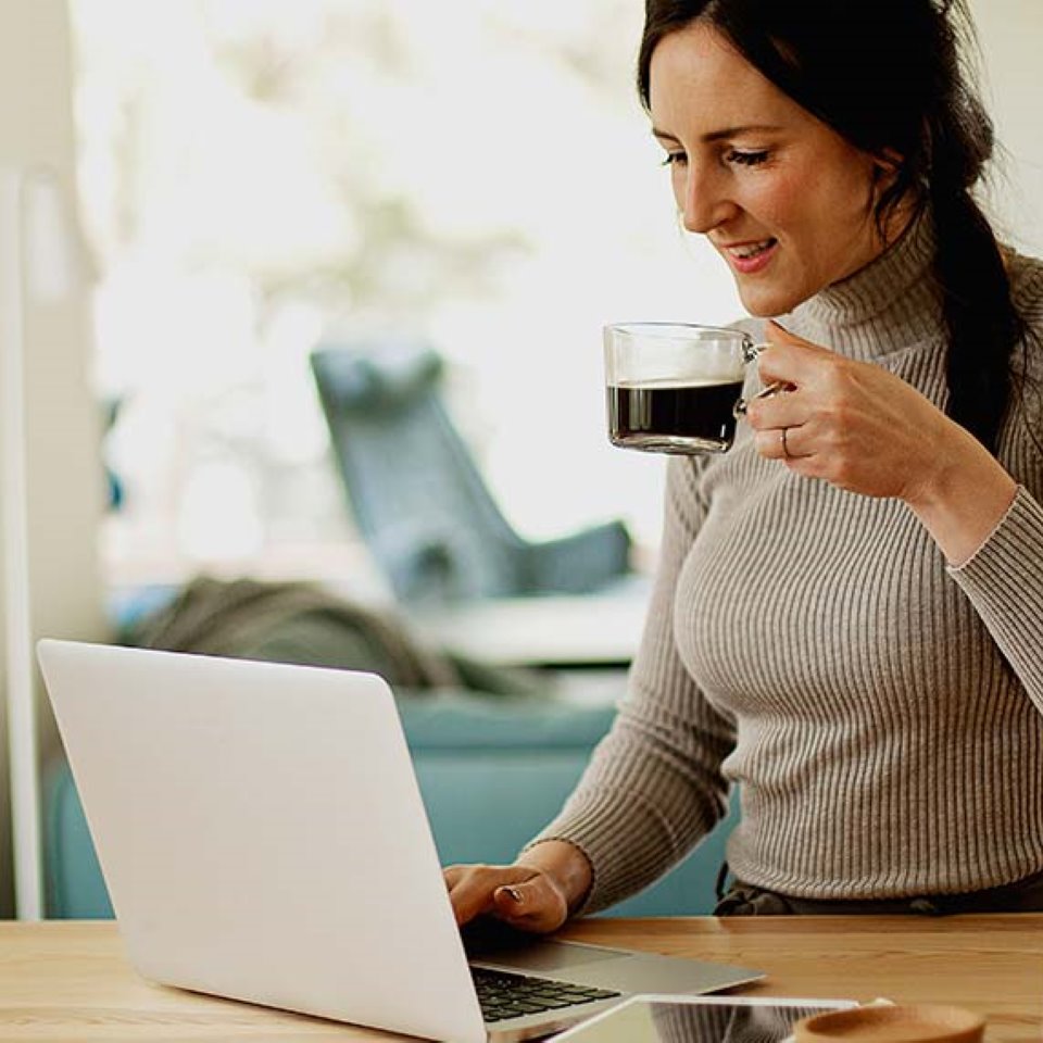 nainen istuu keittiön pöydän ääressä ja käyttää kannettavaa tietokonetta