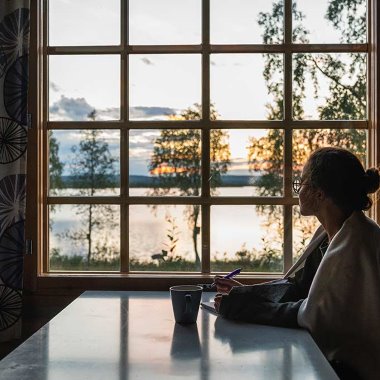 nainen istuu mietteliäänä kesämökillä ikkunan äärellä