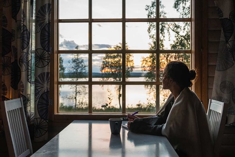 nainen istuu mietteliäänä kesämökillä ikkunan äärellä