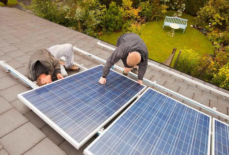 kaksi miestä asentaa aurinkopaneeleita talon katolle