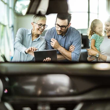 Perhe valitsee autoa liikkeessä myyjän kanssa